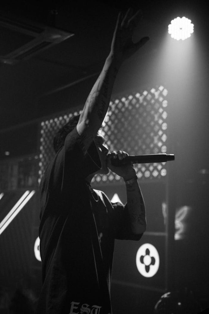 Black and white image of a tattooed musician performing passionately on stage.